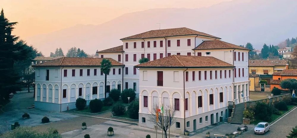 The CIMBA campus buildings in Paderno del Grappa at sunset, with mountains behind